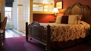 A bedroom with a wooden bed, a nightstand, a lamp, and a window with blinds. - St. Brendan's Inn (Green Bay)