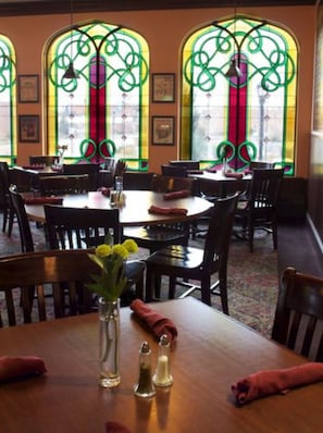 A dining area with round tables and chairs, a vase with flowers, and a window with green ironwork.