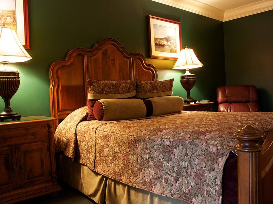 A neatly made bed with floral bedding, two bedside lamps, a wooden headboard, and a framed picture on the wall.