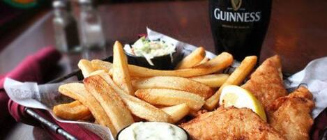 Ein Gericht aus Fisch und Pommes, dazu ein Klecks Remoulade und ein Glas Guinness auf einer Holztischplatte.