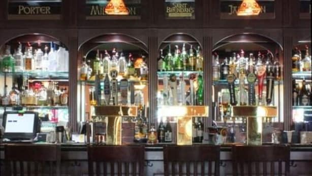 A bar area with wooden chairs, a counter with a cash register, and shelves stocked with various bottles. - St. Brendan's Inn (Green Bay)