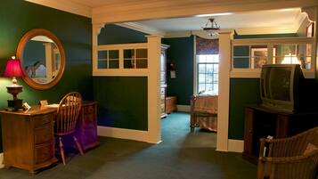 A room with a green wall, a wooden desk with drawers, a chair, a television on a stand, and a window with curtains.
