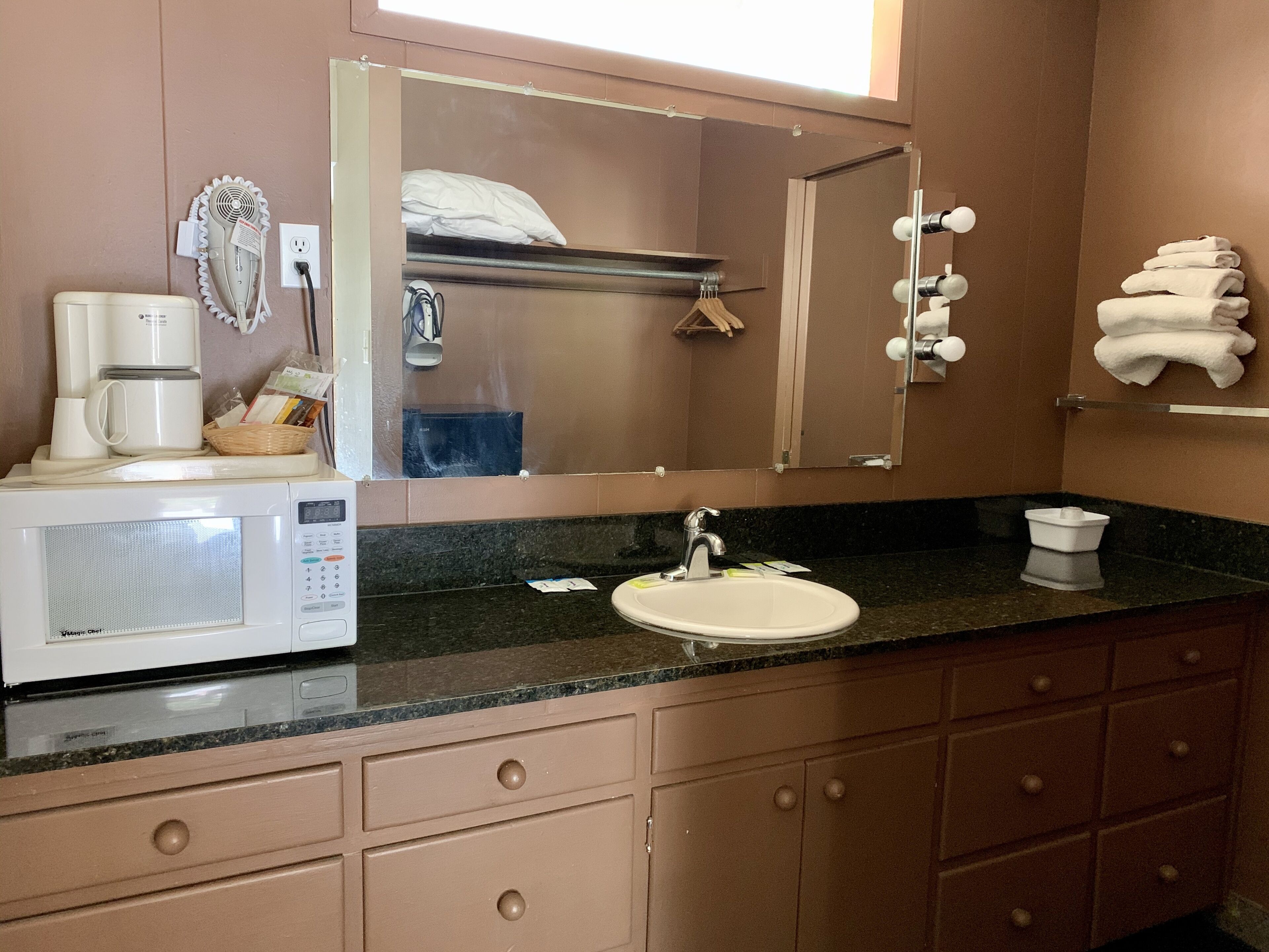 Un bagno con lavandino, specchio e forno a microonde sul piano di lavoro.