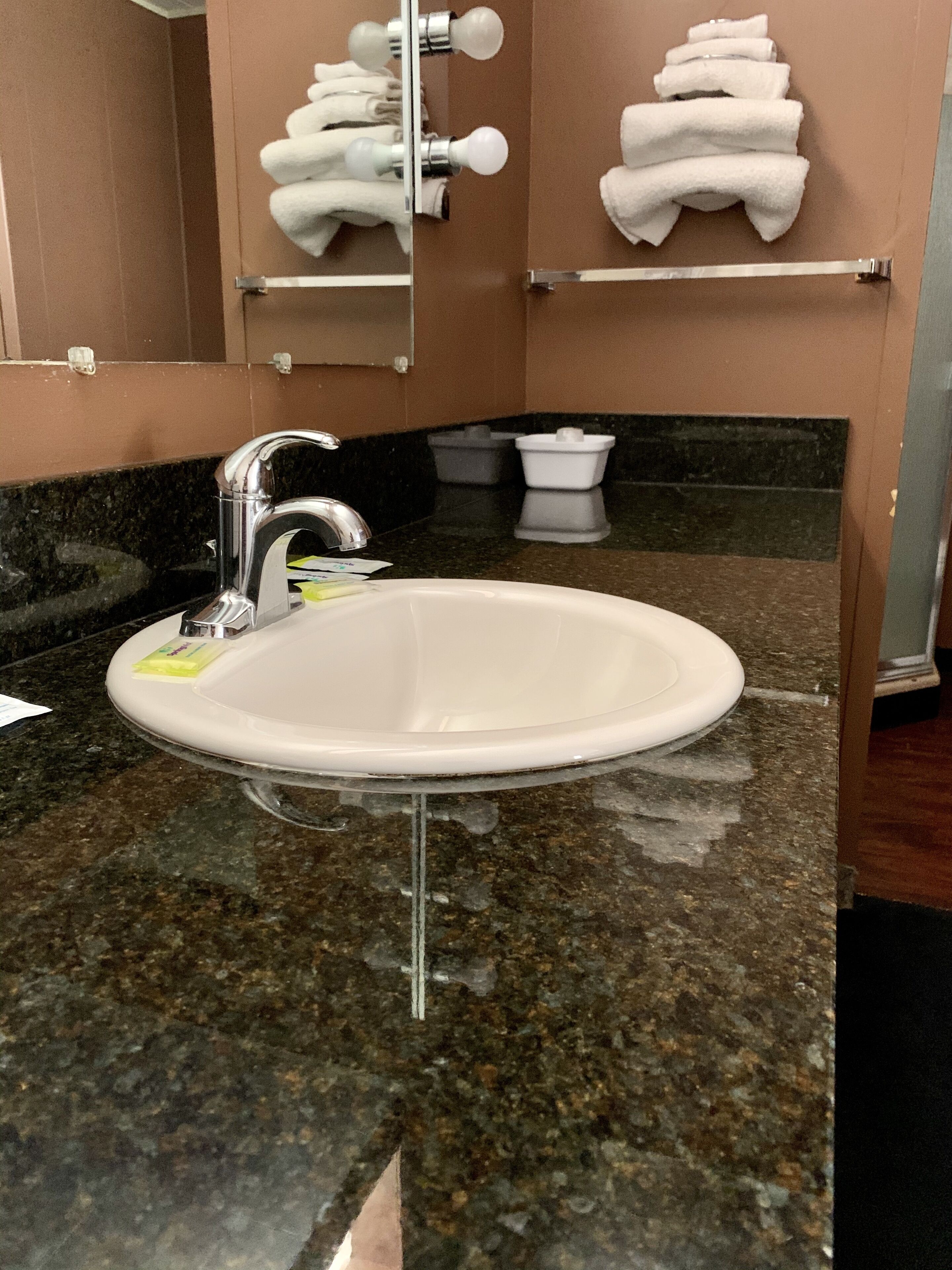 A bathroom with a granite countertop, a white sink, a chrome faucet, and a towel rack with folded towels.