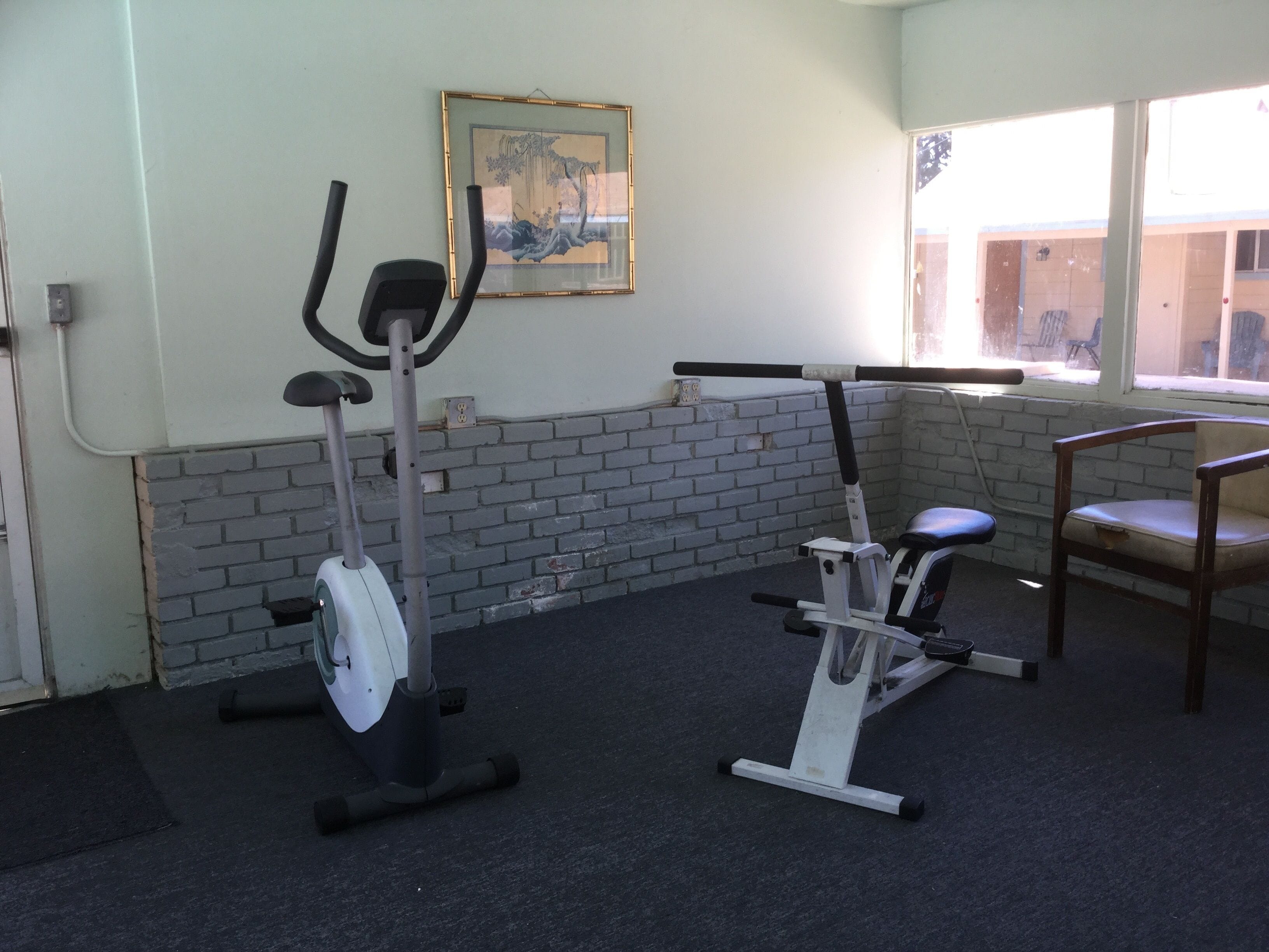 A gym with two stationary bikes, a wall-mounted picture, and a window with a view of the outside.