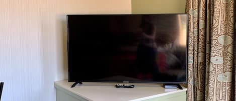 A television on a white cabinet in a room with patterned curtains and a plain wall.