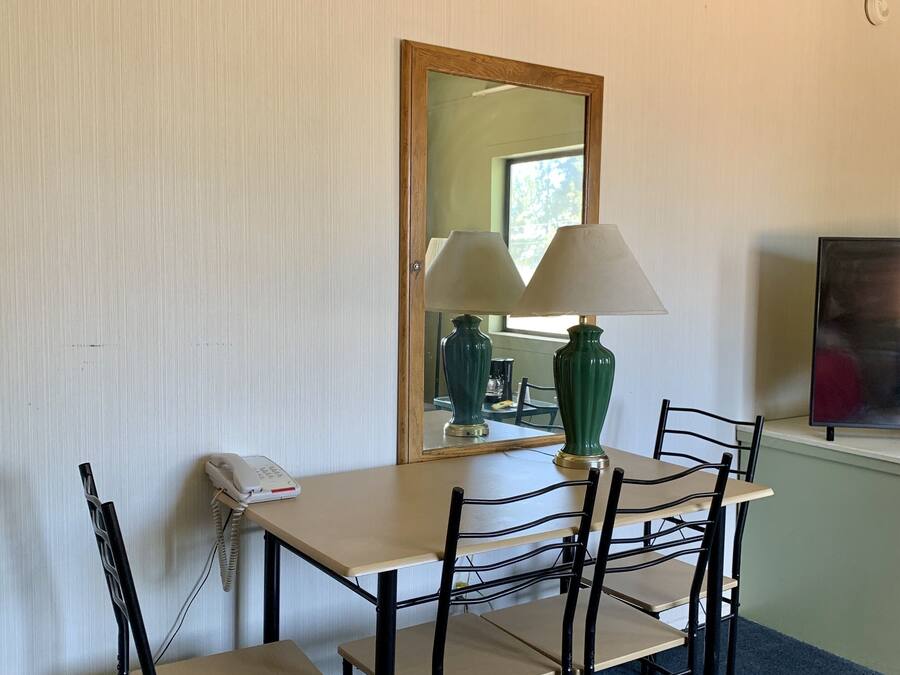 A room with a wooden table, four chairs, a lamp, a phone, and a mirror.
