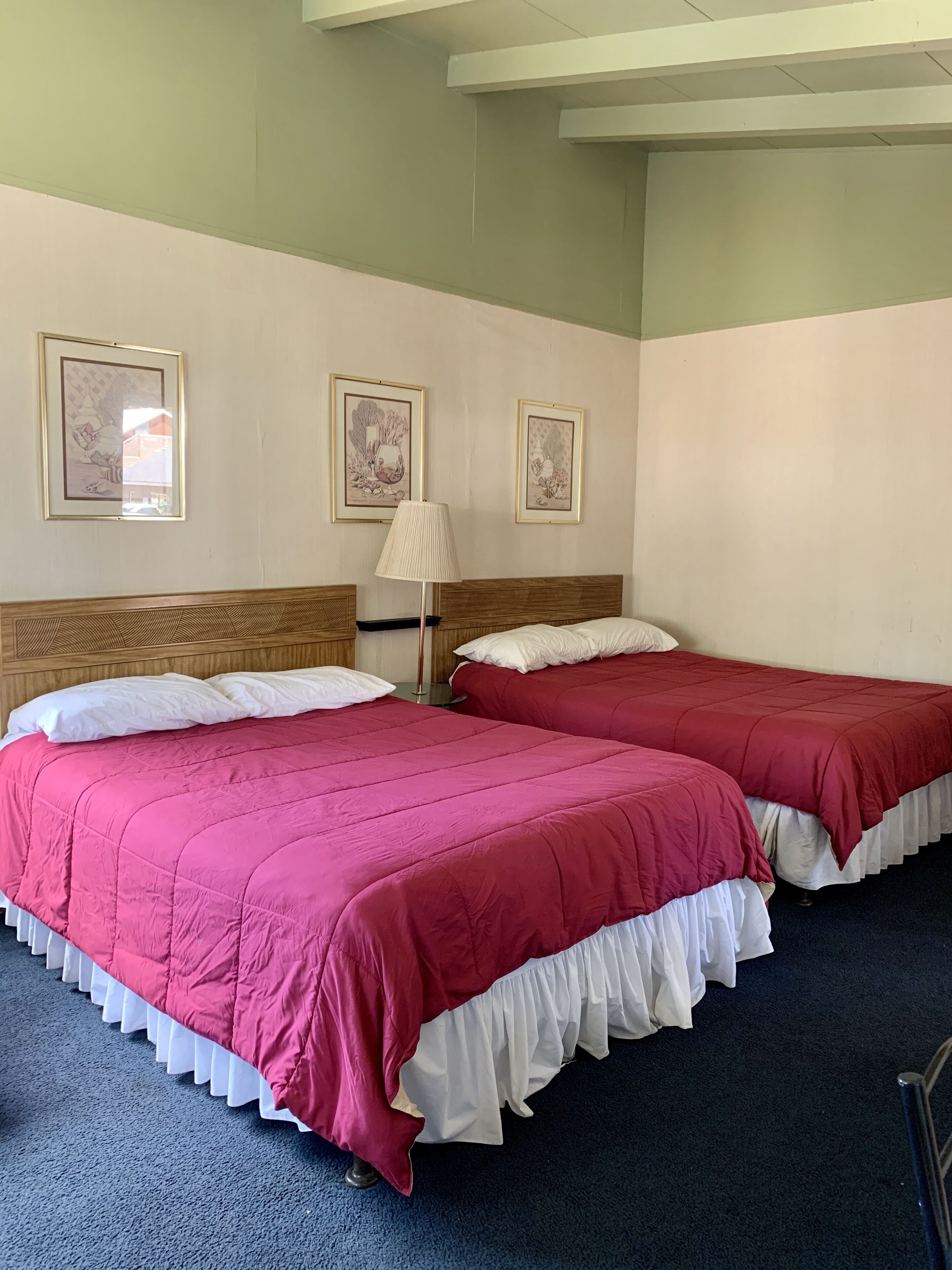 A room with two beds, each with a red bedspread and white pillows, a wooden headboard, and a floor lamp.