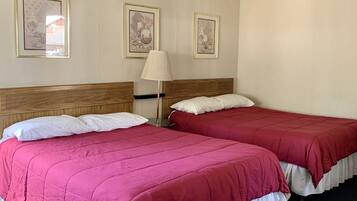 A room with two beds, each with a red bedspread and white pillows, a wooden headboard, and a floor lamp.