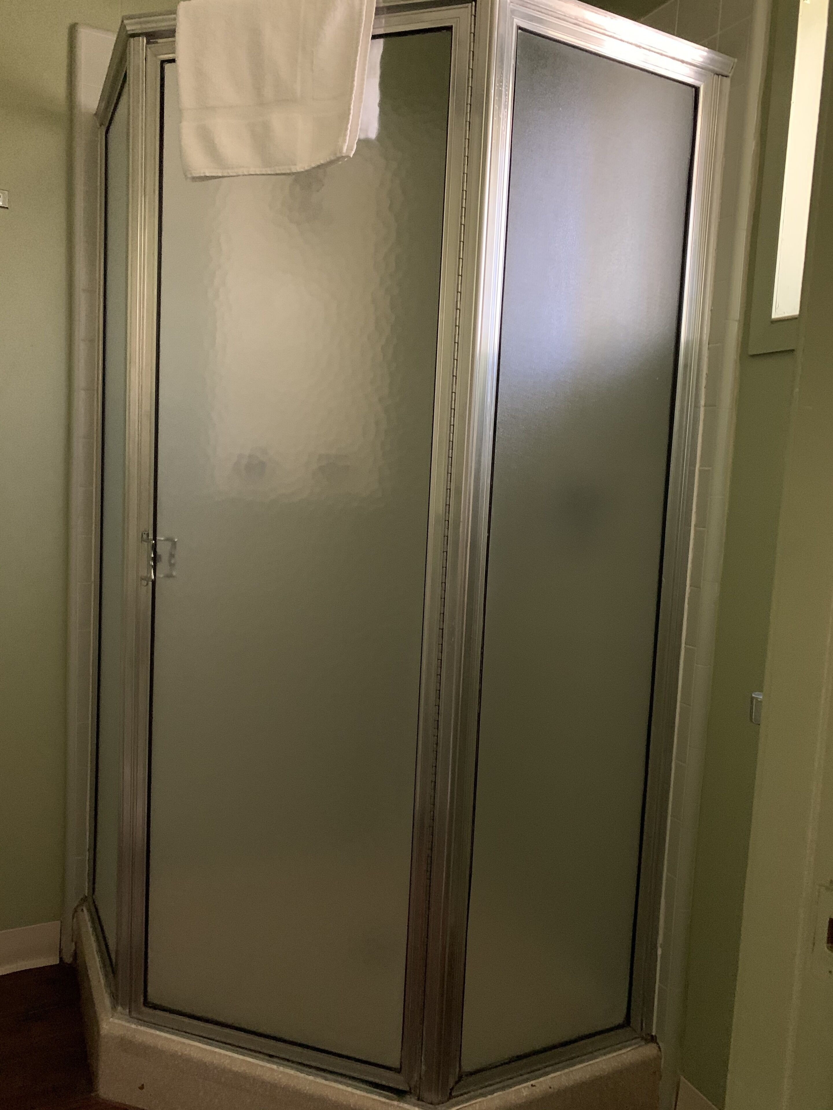 Une douche fermée par des parois de verre, avec une serviette blanche accrochée à la porte.
