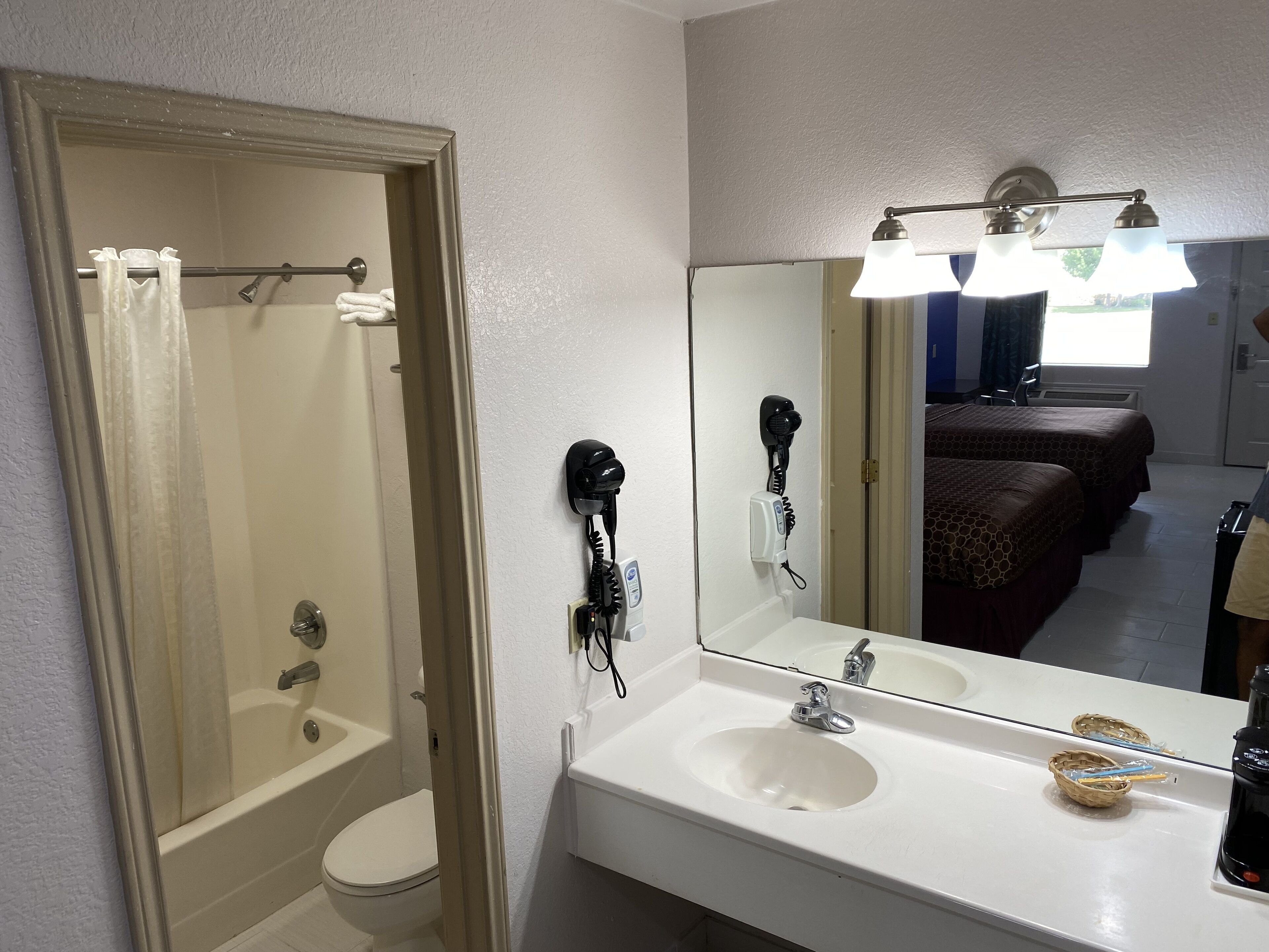 A bathroom with a toilet, a sink, and a mirror. There is a shower curtain and a hairdryer on the wall.