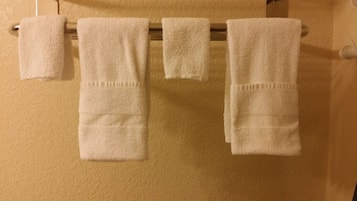A set of four white towels hanging on a metal rack against a textured beige wall.