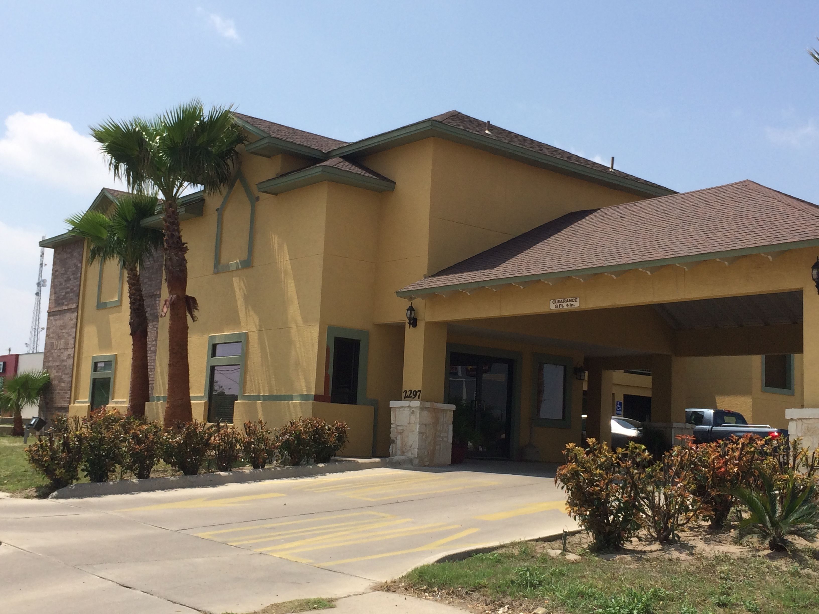 A two-story building with a yellow facade, a covered entrance, and a palm tree in the foreground.