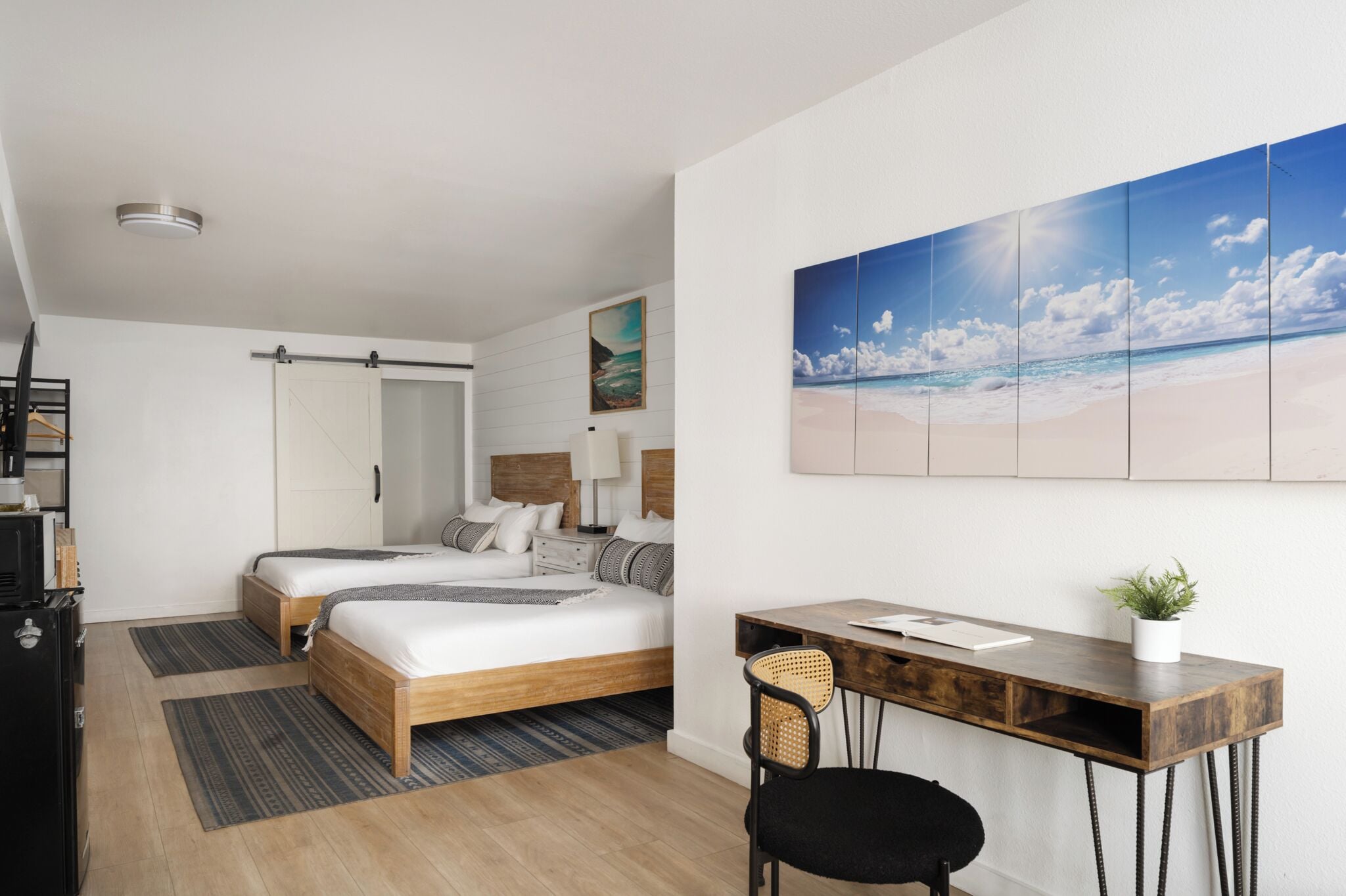 Una habitación de hotel moderna con dos camas, un escritorio y un mural grande con motivos playeros.