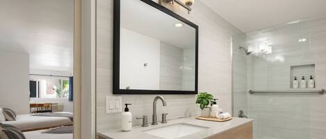 Un baño moderno con un espejo grande, un lavamanos y una ducha.