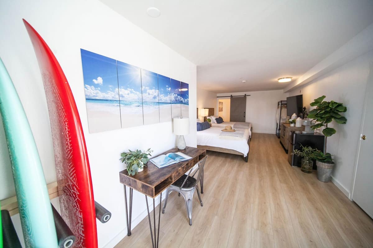 A hotel room with a bed, desk, and a large beach mural on the wall.