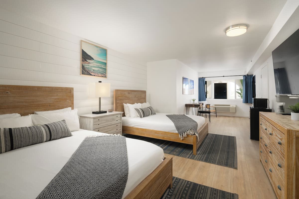 A hotel room with two beds, a desk, a television, and a view of the ocean.