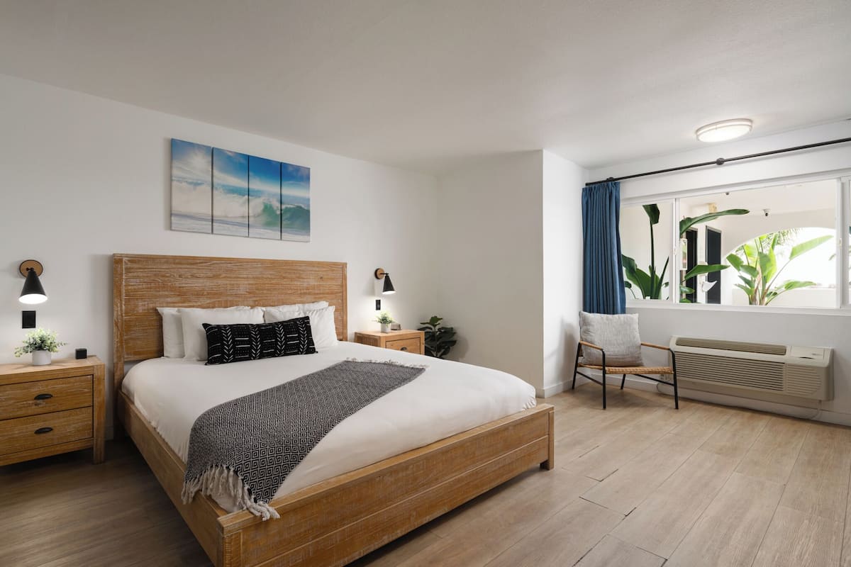 A modern bedroom with a wooden bed, bedside tables with lamps, a window with curtains, and a wall-mounted air conditioner.