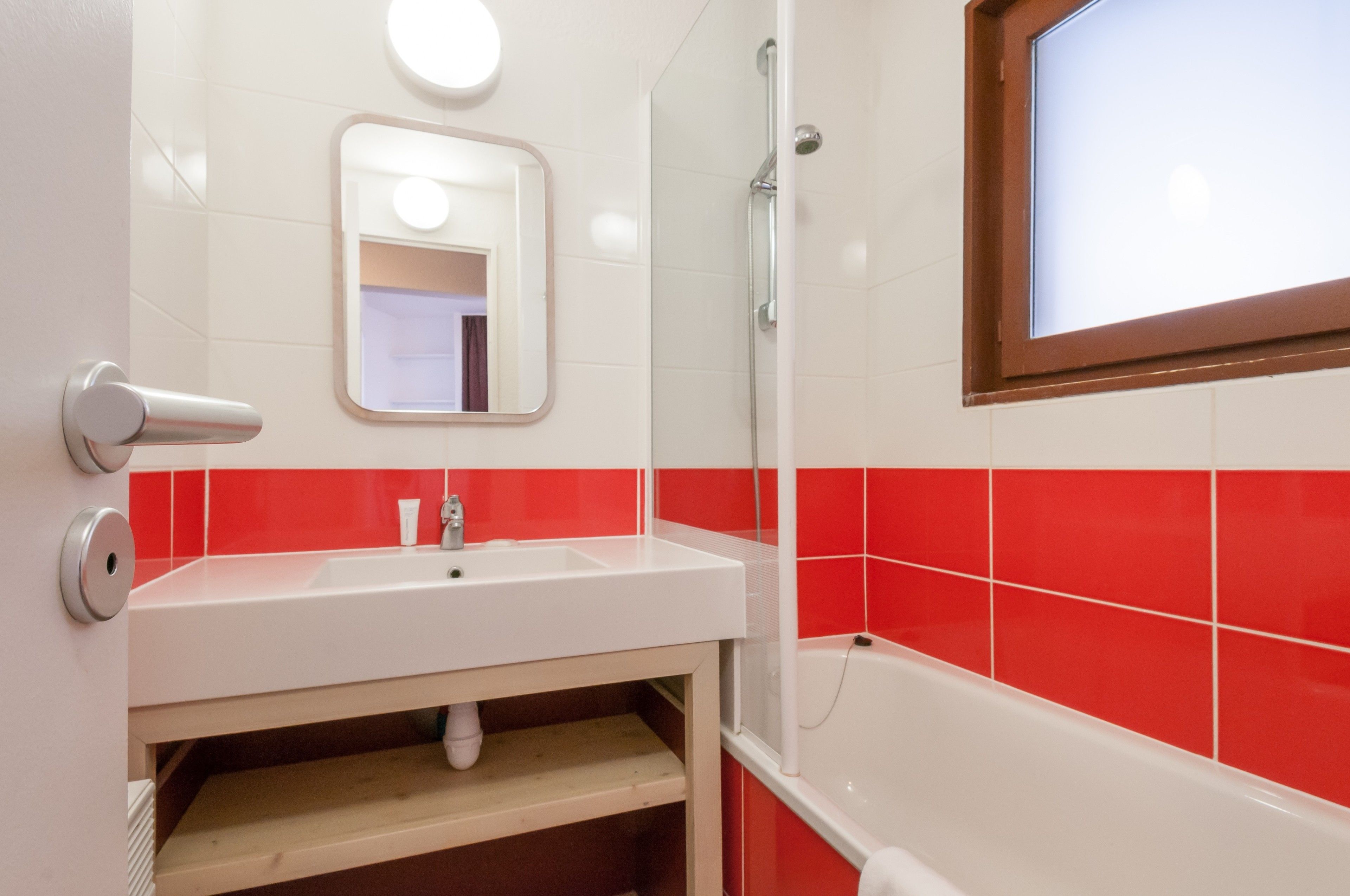 A bathroom with a white sink, red-tiled walls, a mirror, and a shower.