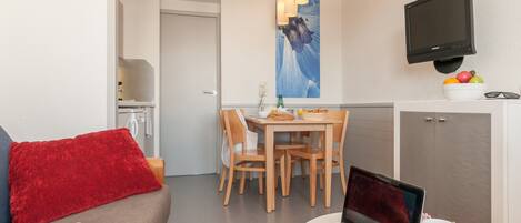 Un salon moderne avec un canapé rouge, un ordinateur portable posé sur une petite table, et un coin repas comprenant une table et des chaises en bois.