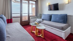 A hotel room with a bed, a sofa, a small table, a TV, and a window with curtains. - Résidence Pierre & Vacances Antarès (Avoriaz)