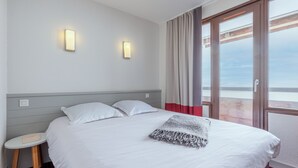 A hotel room with a bed, two wall-mounted lights, a small table, and a view through a large window. - Résidence Pierre & Vacances Antarès (Avoriaz)