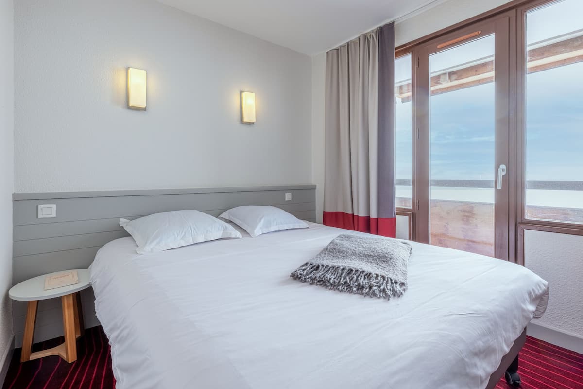 Ein Hotelzimmer mit einem Bett, zwei Wandleuchten, einem kleinen Tisch und Blick durch ein großes Fenster.