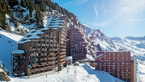 A ski resort with multiple buildings, including a large wooden structure and a red building with balconies, surrounded by snow-covered mountains. - Résidence Pierre & Vacances Antarès (Avoriaz)
