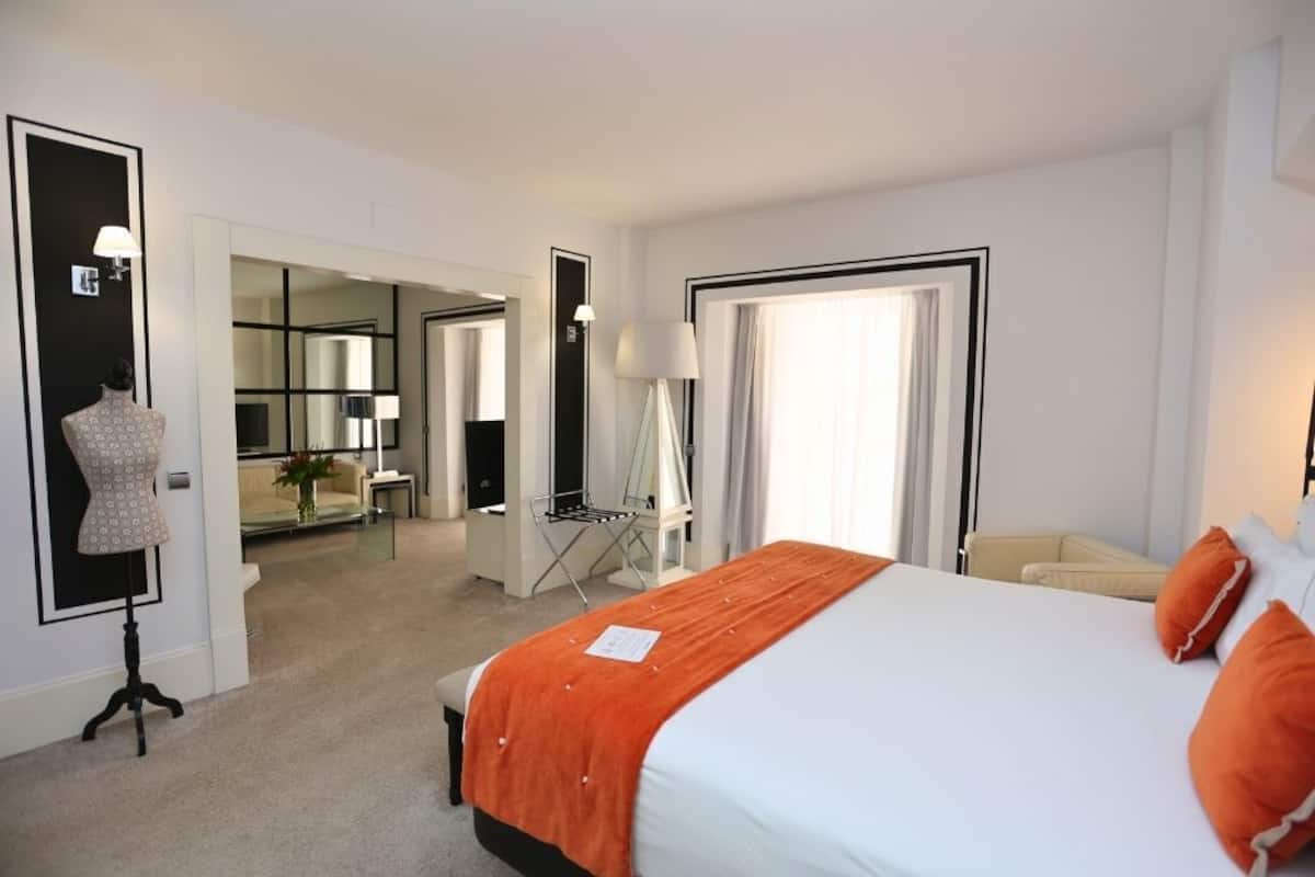 Habitación de hotel con una cama grande, un escritorio y una silla. Se observa un espejo y una lámpara en la pared.