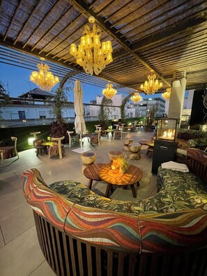 Un patio al aire libre con asientos acolchados, una chimenea y múltiples lámparas colgantes.