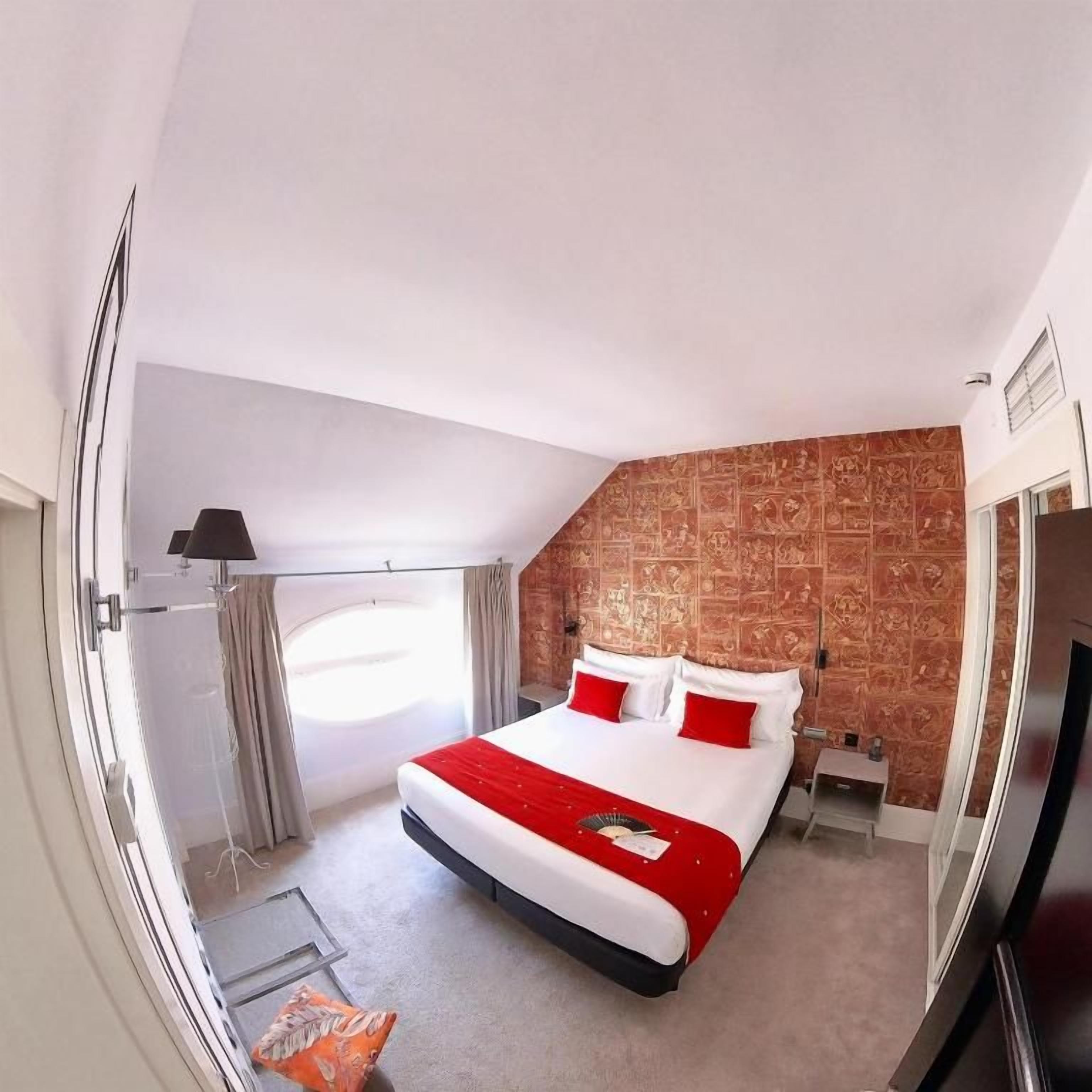 A hotel room with a bed, a nightstand, a lamp, and a window.
