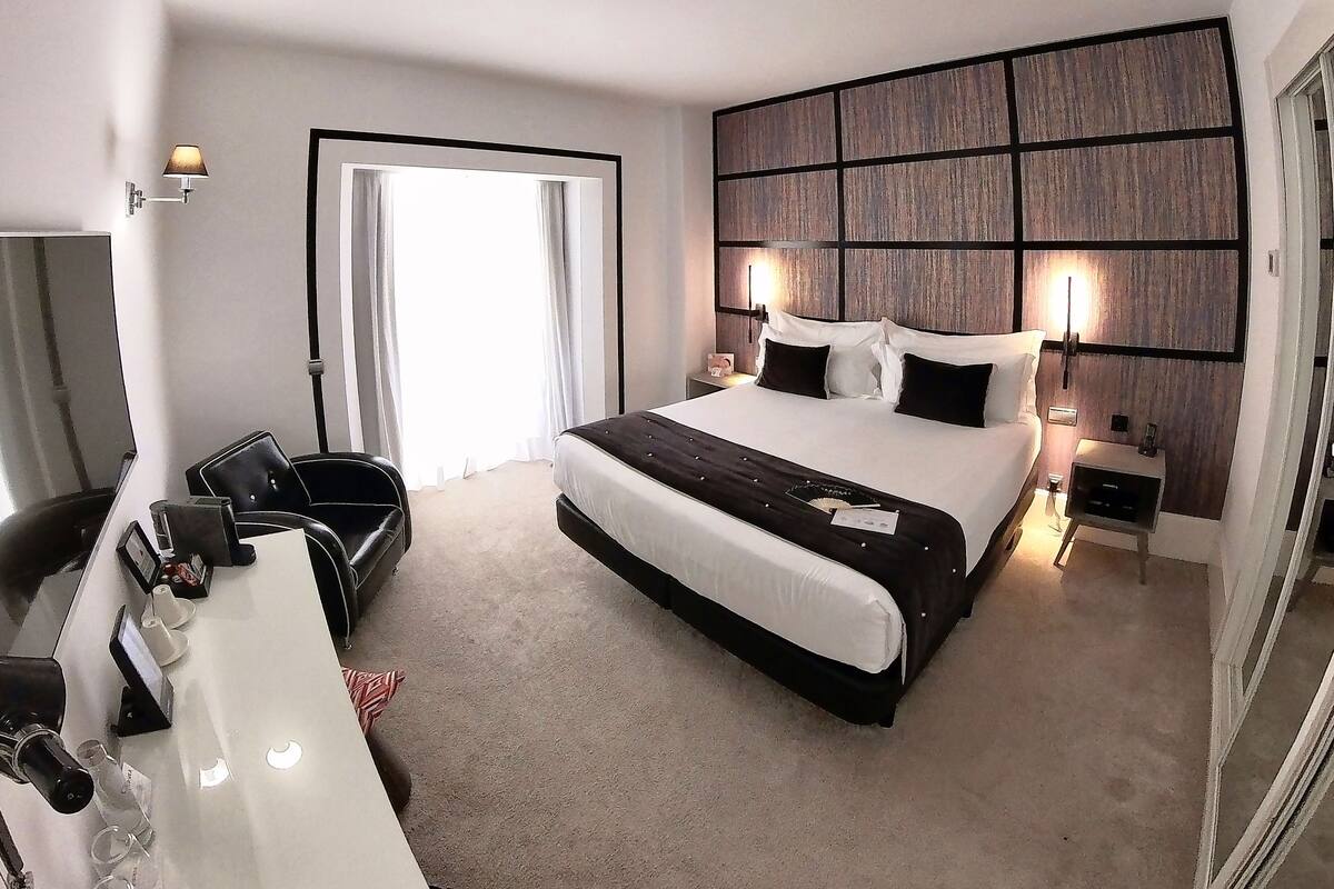 Una habitación de hotel moderna con una cama grande, mesitas de noche, un escritorio y un espejo.
