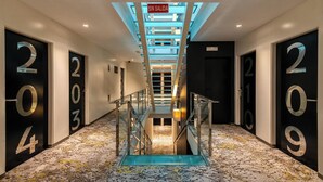 A modern hotel hallway with a glass staircase, numbered doors, and a 'SIN SALIDA' sign. - Mariposa Hotel Malaga (Málaga)