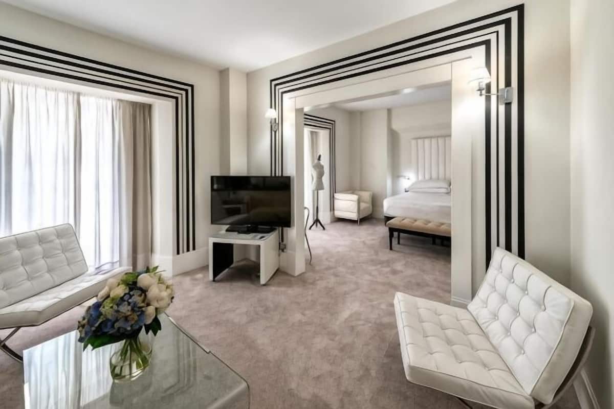 A hotel room with a sofa, a TV, a bed, and a mirror.