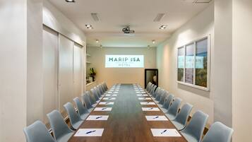 A conference room with a long table, chairs, and a projector screen displaying "MARIPOSA HOTEL".