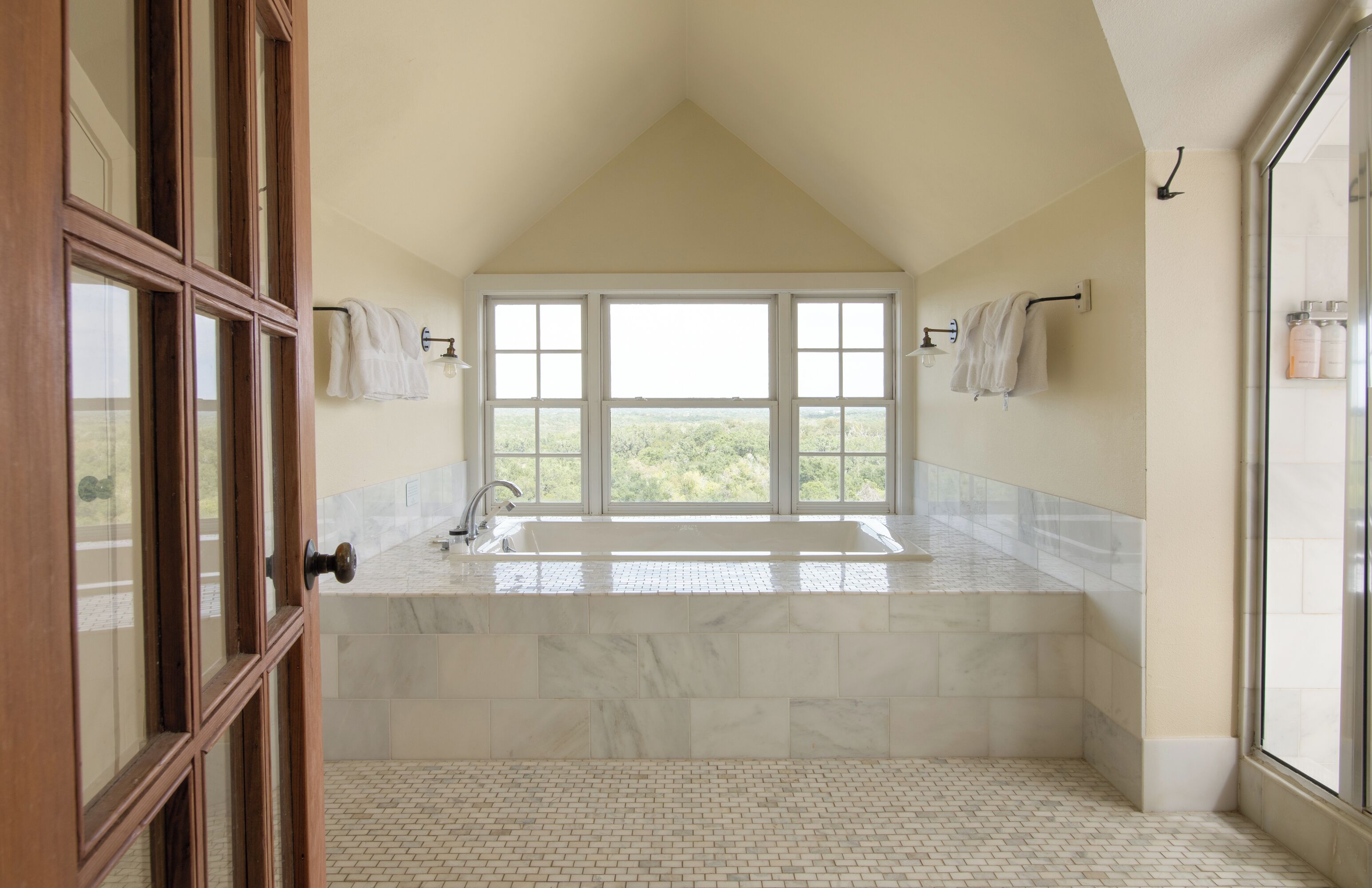 A spacious bathroom with a large window, a bathtub, and a shower area.