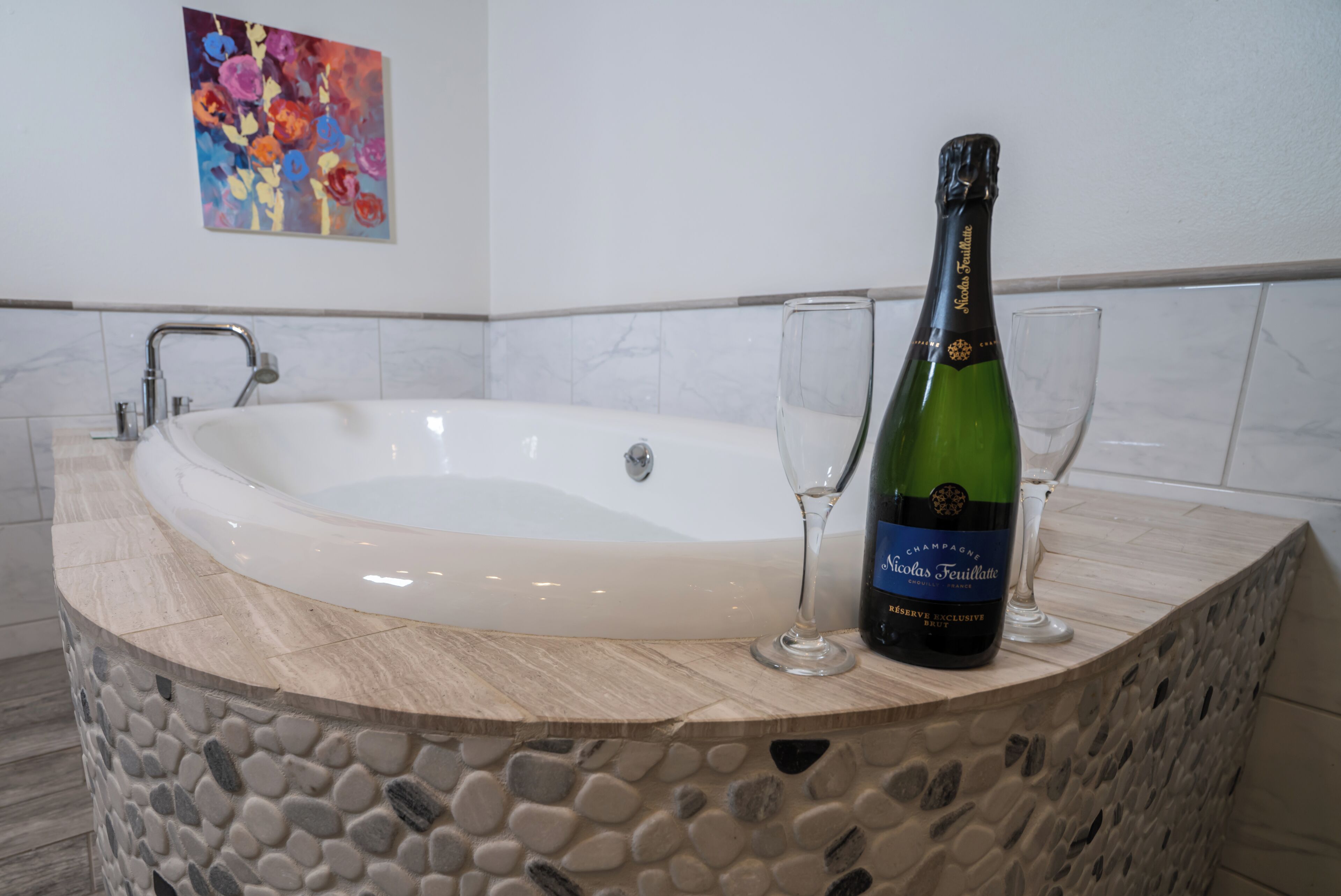 Una bañera con revestimiento de piedra, una botella de champán y dos copas sobre una encimera de mármol.