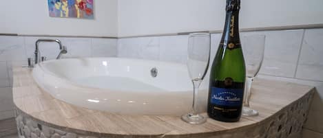 Una bañera con revestimiento de piedra, una botella de champán y dos copas sobre una encimera de mármol.
