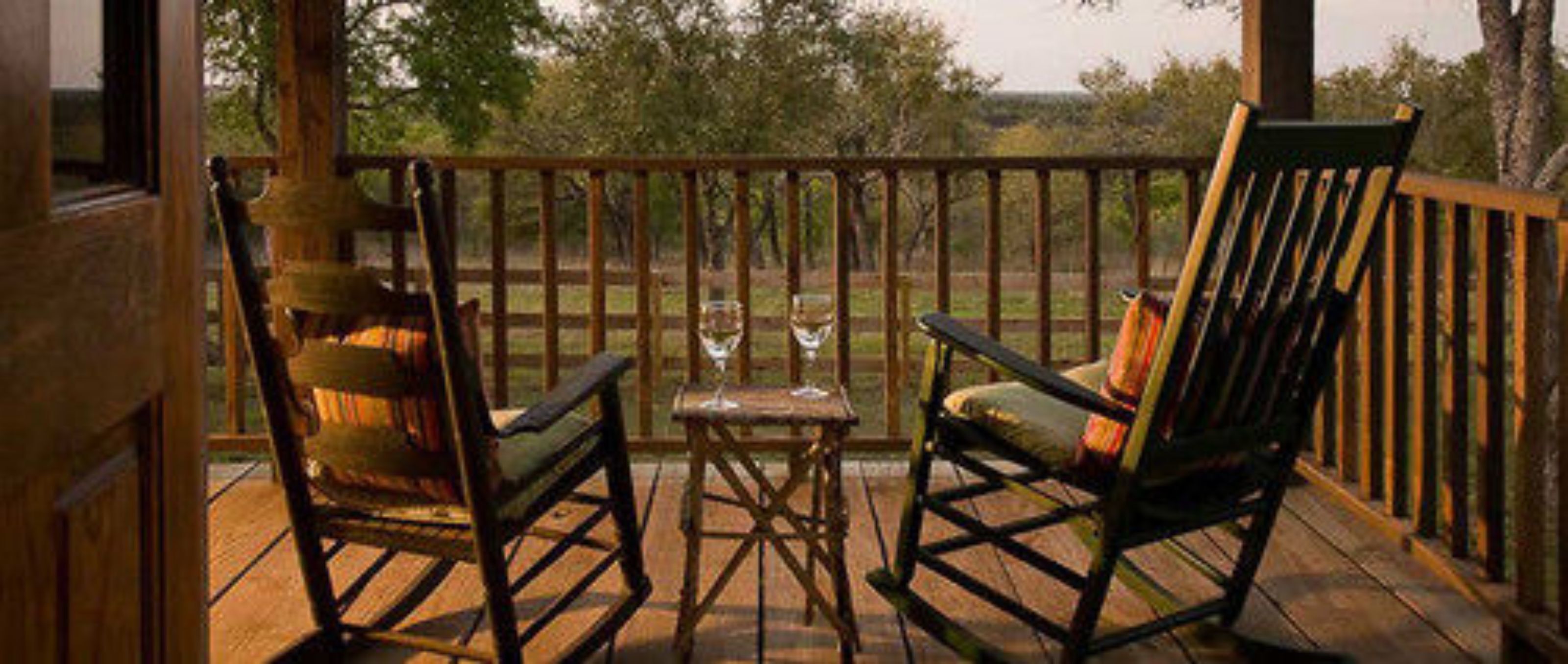 A wooden deck with two rocking chairs and a small table, overlooking a grassy area.