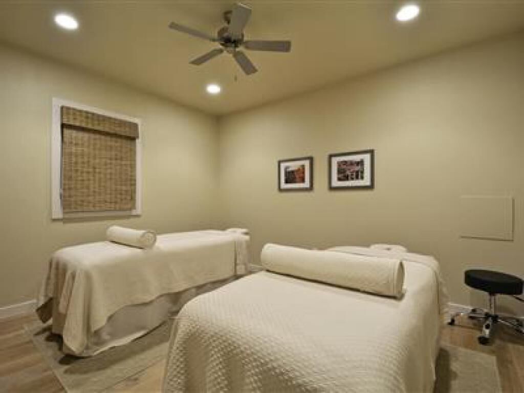 A room with two beds covered in white linens, a ceiling fan, and two framed pictures on the wall.