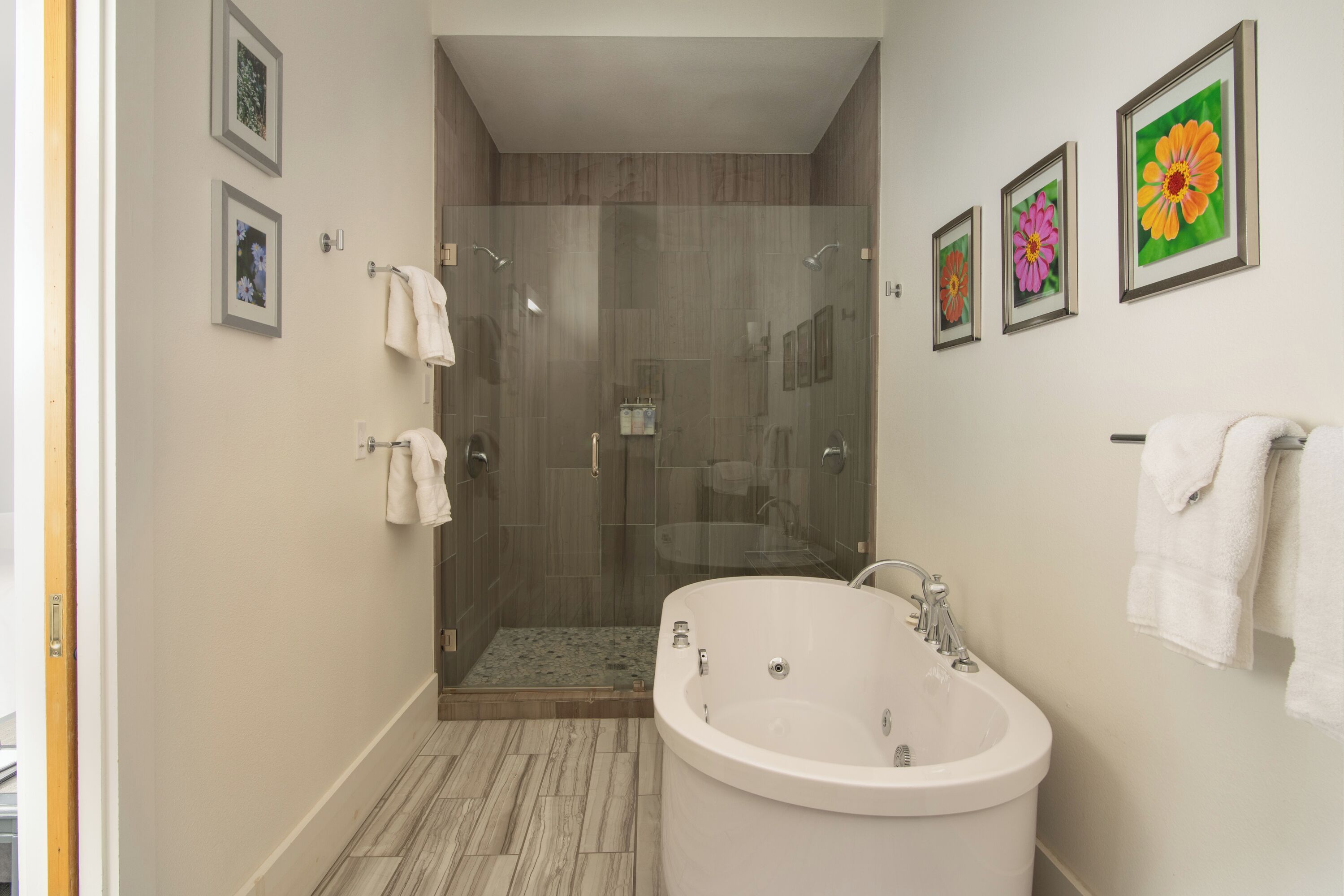 A modern bathroom with a glass-enclosed shower, a freestanding bathtub, and framed floral artwork on the walls.