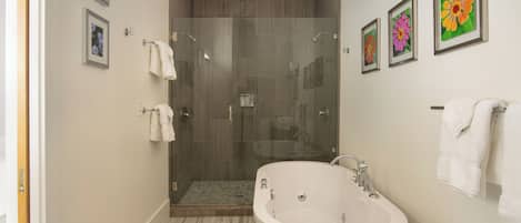 A modern bathroom with a glass-enclosed shower, a freestanding bathtub, and framed floral artwork on the walls.