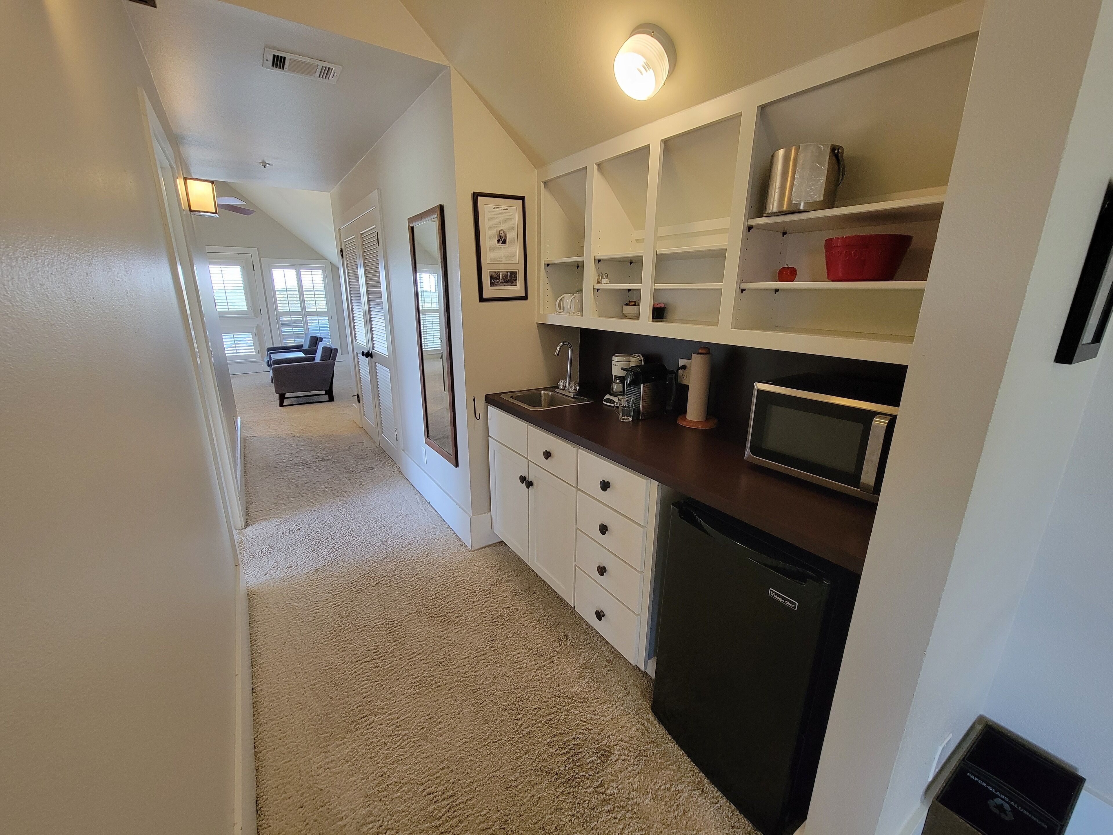 A compact kitchen with white cabinets, a microwave, and a coffee maker. A small refrigerator is also visible.