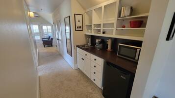 A compact kitchen with white cabinets, a microwave, and a coffee maker. A small refrigerator is also visible.