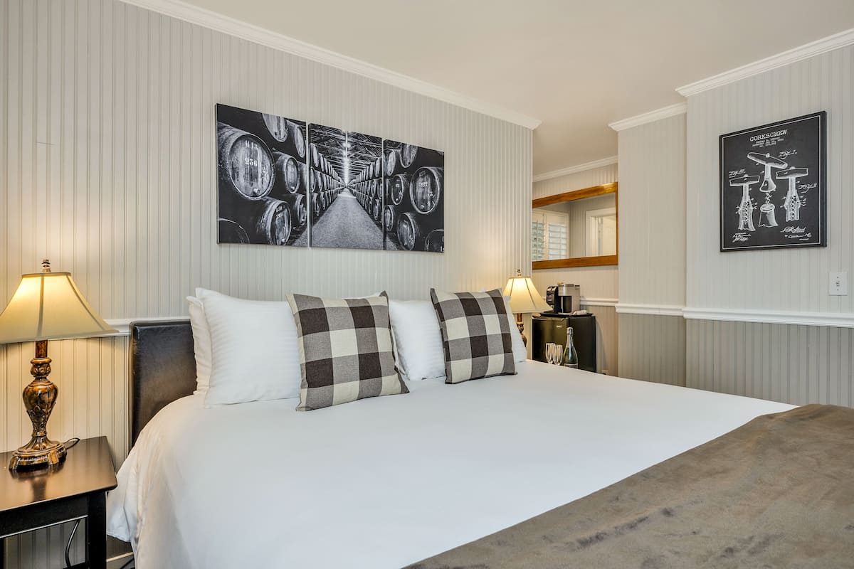 A hotel room with a large bed, two bedside tables with lamps, a checkered pillow set, and a wall art piece depicting barrels.