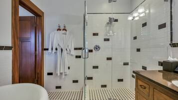 A bathroom with a glass-enclosed shower, a white bathtub, and a wooden vanity with a sink.