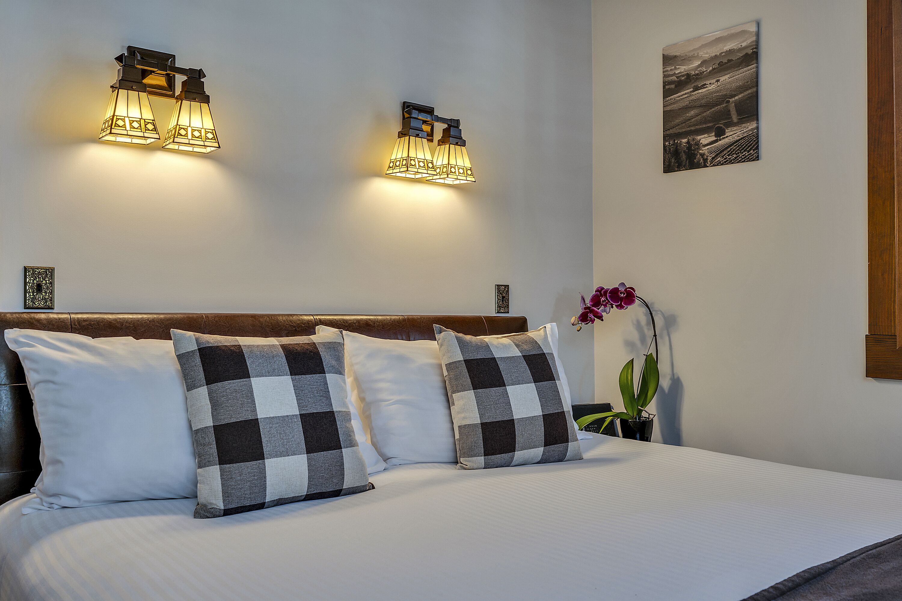 A neatly made bed with two pillows, a headboard, and wall-mounted lighting fixtures.