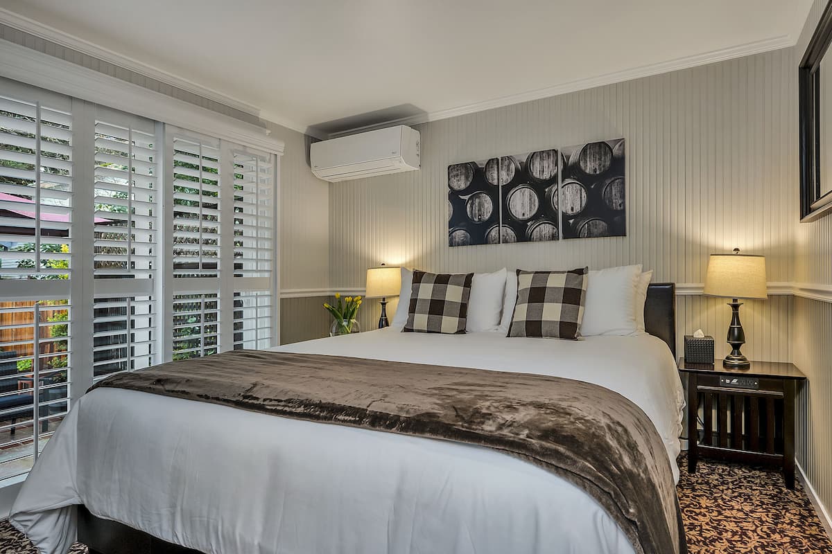 A hotel room with a large bed, two bedside lamps, a wall-mounted air conditioner, and a window with blinds.