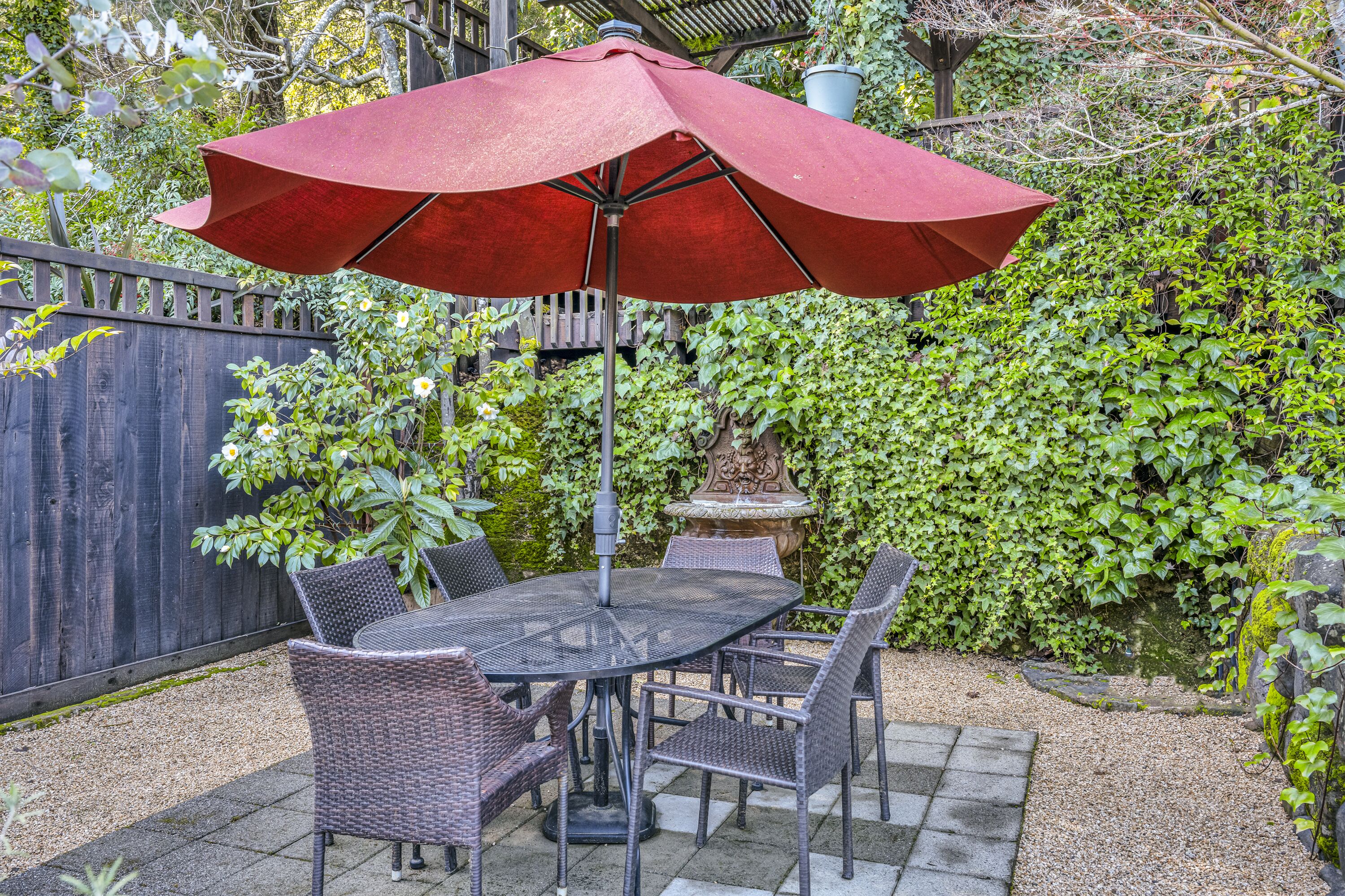 A patio with a table and chairs, a red umbrella, and a wooden fence.
