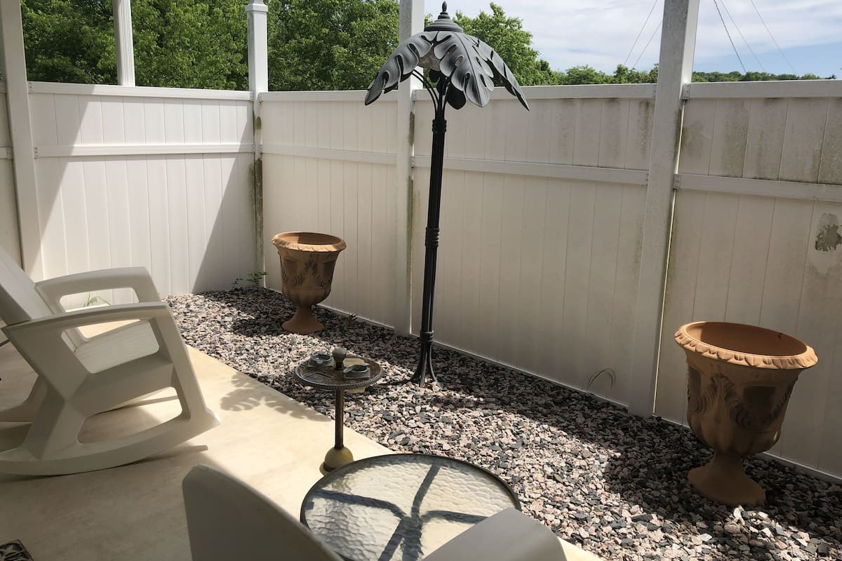 A patio area with a white chair, a table with a glass top, a decorative metal lamp, and two terracotta pots.